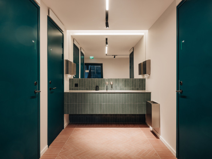 Washroom with a green-tiled basin wall and reddish flooring at Nortal office
